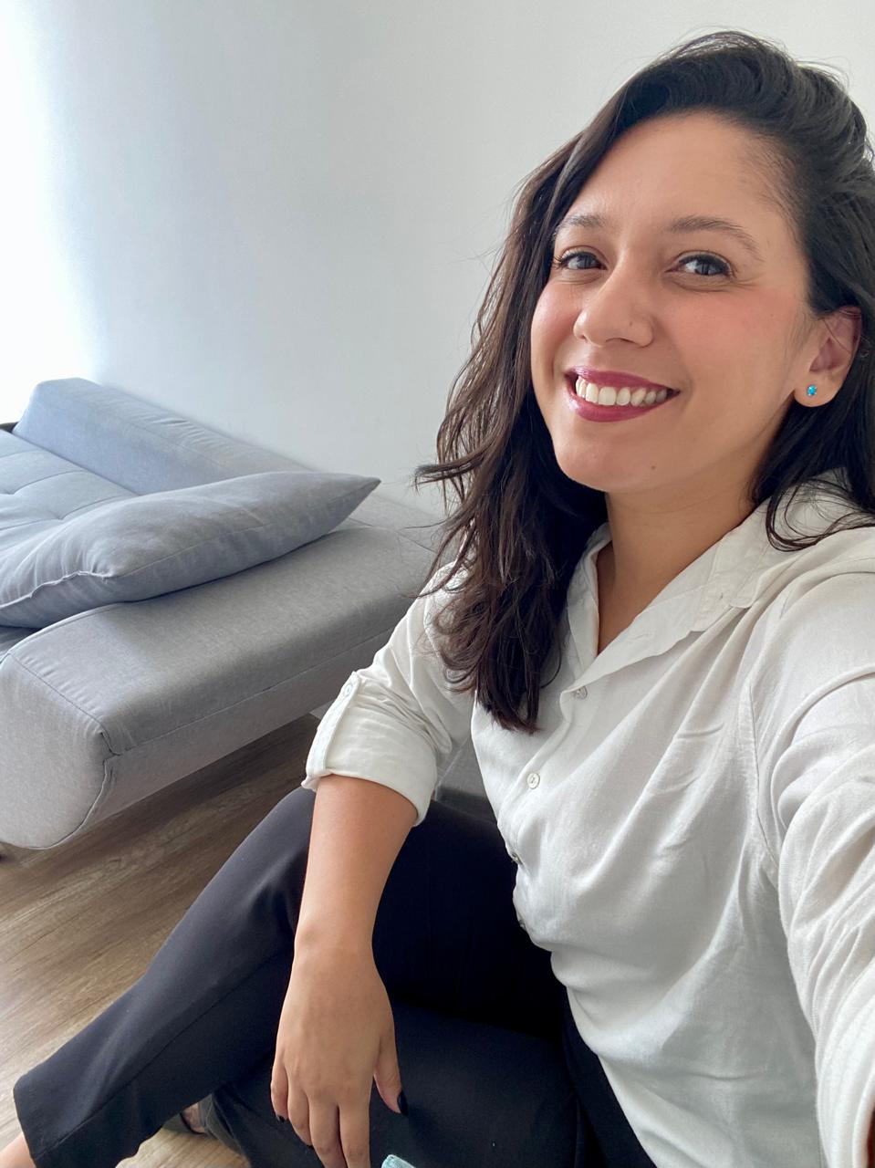 Tatiane Domingues, de camisa branca, sorrindo, sentada no consultório